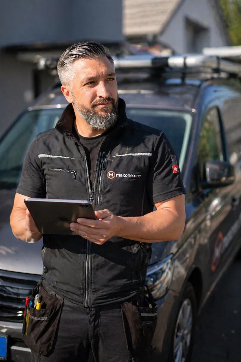 Max Karastelev im maxone.one-Arbeitsvest mit Tablet vor seinem Firmenwagen